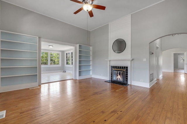 unfurnished living room featuring hardwood / wood-style floors, a tiled fireplace, a ceiling fan, and arched walkways