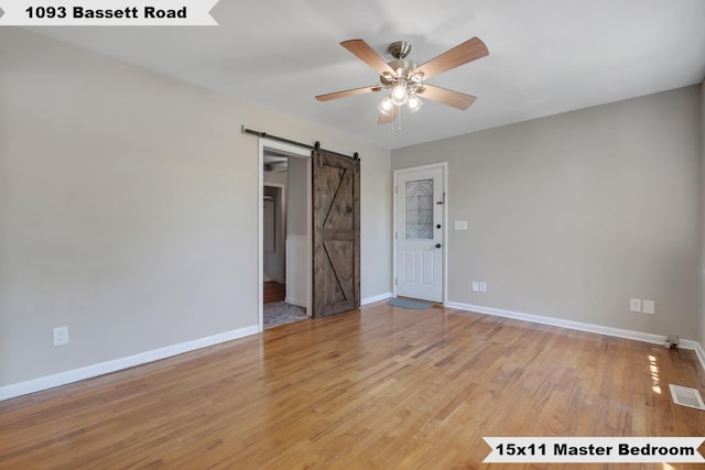 empty room featuring visible vents, baseboards, a barn door, light wood-type flooring, and a ceiling fan