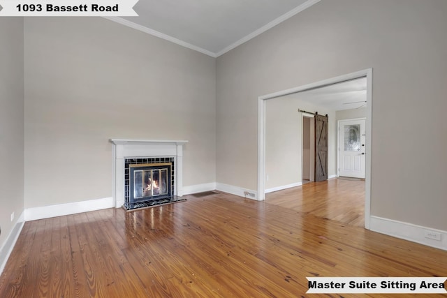 unfurnished living room with crown molding, baseboards, a barn door, and wood finished floors