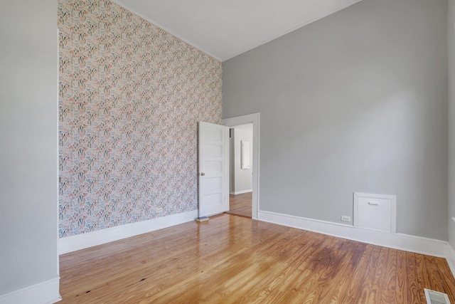 spare room with visible vents, baseboards, wood finished floors, and wallpapered walls