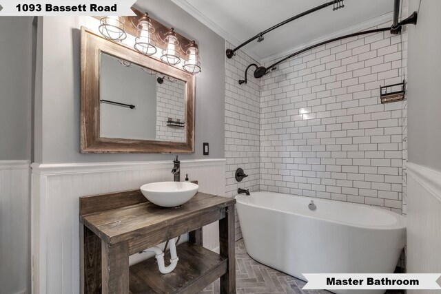 full bath featuring a sink, ornamental molding, wainscoting, and shower / washtub combination