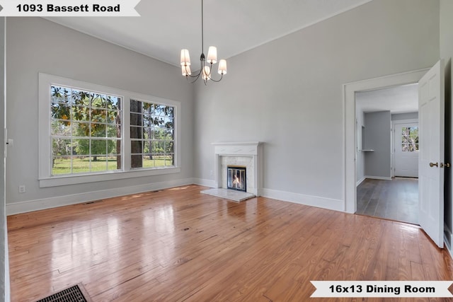 unfurnished living room with a notable chandelier, baseboards, visible vents, wood-type flooring, and a premium fireplace