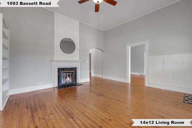 unfurnished living room with arched walkways, a ceiling fan, visible vents, a tile fireplace, and hardwood / wood-style flooring