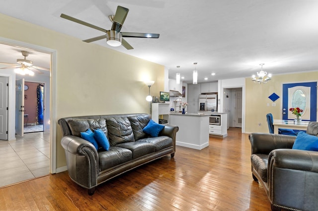 living room with ceiling fan with notable chandelier and light hardwood / wood-style flooring