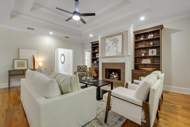 3574 Strolling Way, Tallahassee, FL 32311 - living area with a tiled fireplace, ceiling fan, crown molding, light wood-style floors, and a raised ceiling