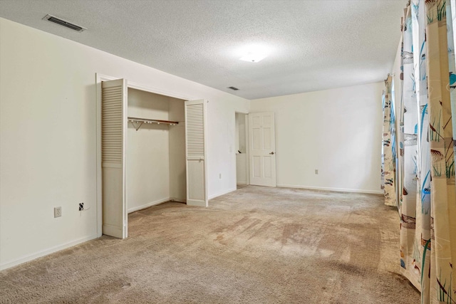 unfurnished bedroom featuring light colored carpet, a textured ceiling, and a closet