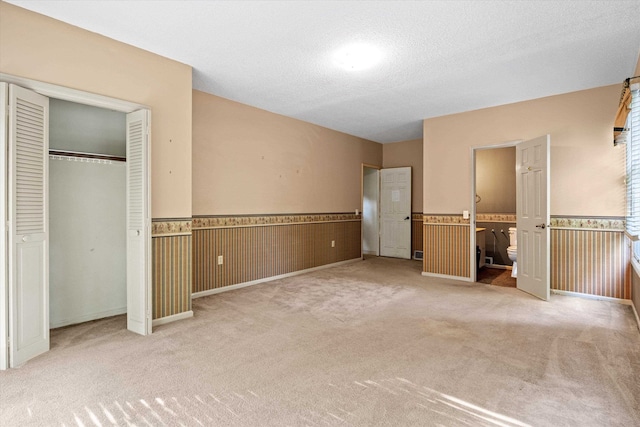 unfurnished bedroom with wood walls, light carpet, ensuite bathroom, a textured ceiling, and a closet