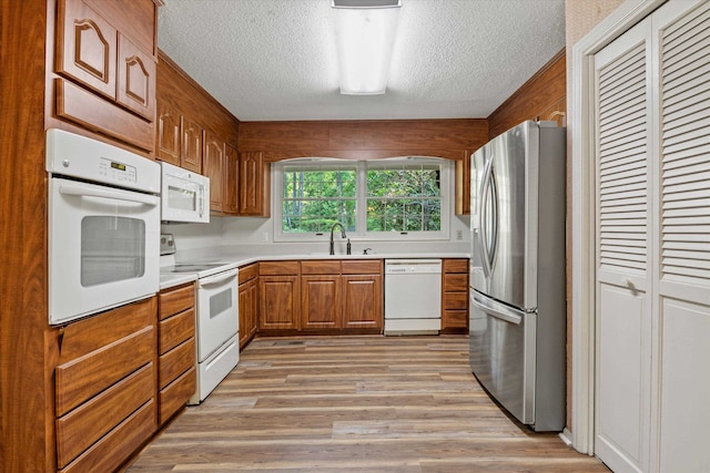 kitchen with white appliances, a textured ceiling, sink, and light hardwood / wood-style flooring