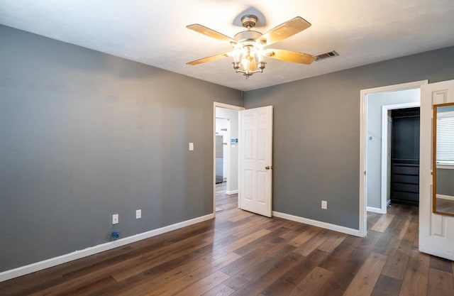 unfurnished bedroom with dark wood-type flooring, a closet, a walk in closet, and ceiling fan