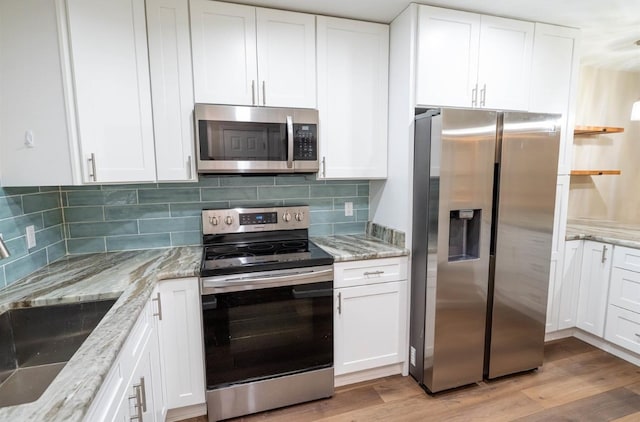 kitchen with white cabinetry, light stone countertops, appliances with stainless steel finishes, and light hardwood / wood-style flooring