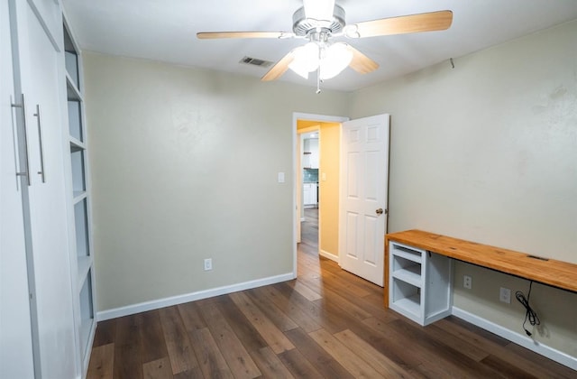 unfurnished office featuring dark wood-type flooring, built in desk, and ceiling fan