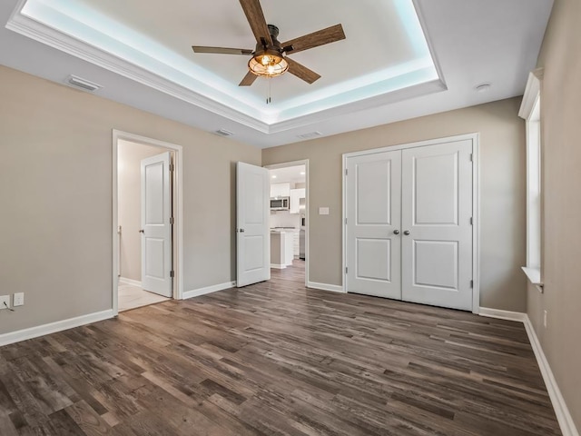 unfurnished bedroom with ceiling fan, a closet, a tray ceiling, and dark hardwood / wood-style floors