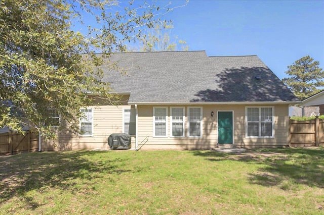 rear view of house featuring a lawn, fence, entry steps, and roof with shingles