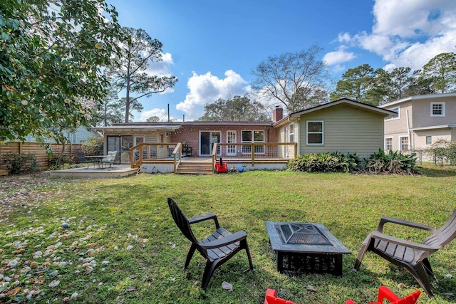 rear view of house with an outdoor fire pit, a deck, and a lawn