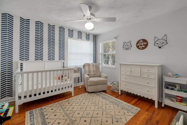 bedroom featuring ceiling fan, wood-type flooring, a nursery area, and a textured ceiling