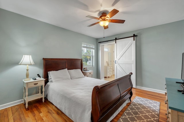 bedroom featuring ceiling fan, a barn door, light wood-type flooring, and ensuite bath