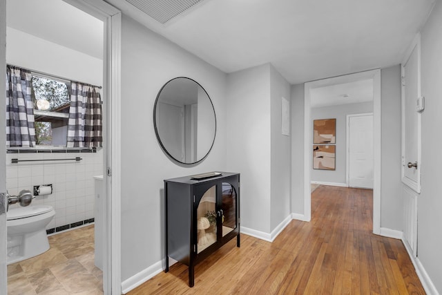 hall with tile walls and light hardwood / wood-style floors