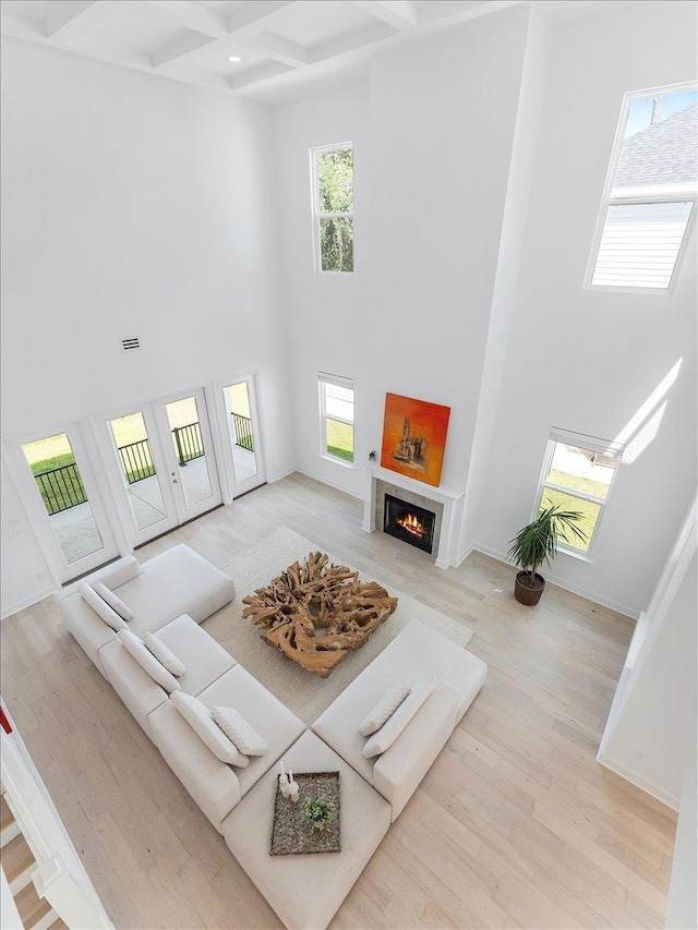 living room featuring a high ceiling, coffered ceiling, beamed ceiling, wood finished floors, and a warm lit fireplace