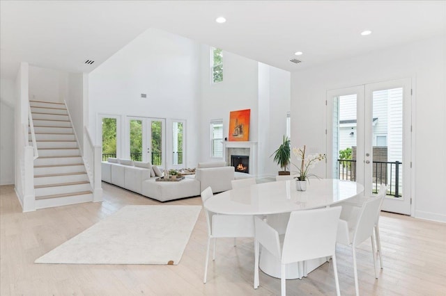 dining room featuring a warm lit fireplace, light wood-style floors, stairs, a towering ceiling, and recessed lighting