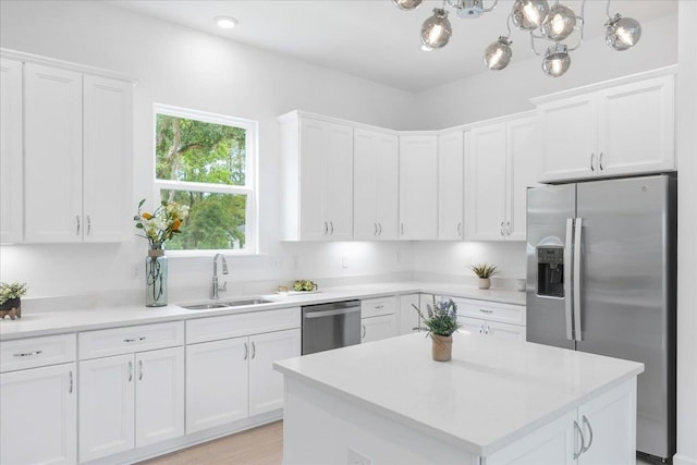 kitchen featuring appliances with stainless steel finishes, a sink, light countertops, white cabinets, and a center island