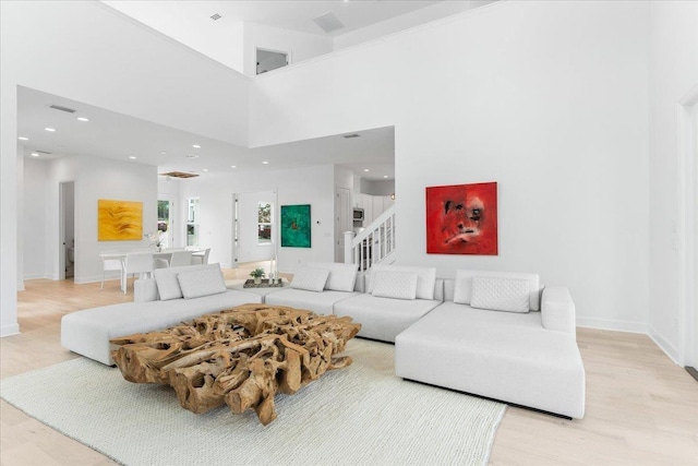 living area featuring light wood-style floors, baseboards, recessed lighting, stairway, and a high ceiling