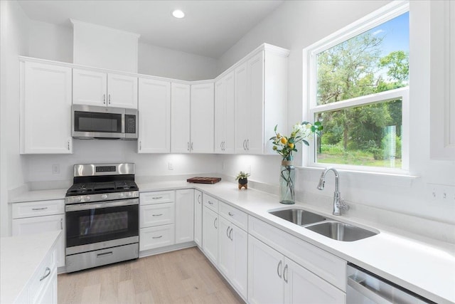 kitchen with stainless steel appliances, a sink, light countertops, white cabinetry, and plenty of natural light