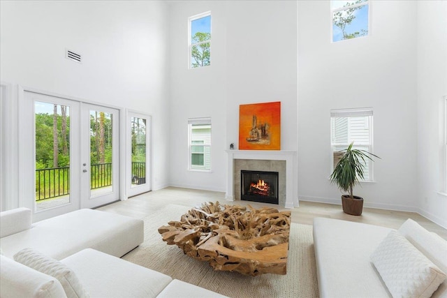 living room featuring a high ceiling, a tiled fireplace, french doors, baseboards, and wood finished floors