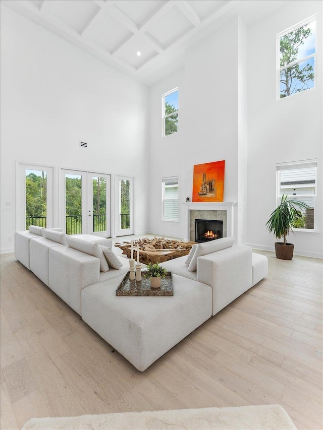 living area featuring a towering ceiling, a lit fireplace, wood finished floors, beam ceiling, and coffered ceiling