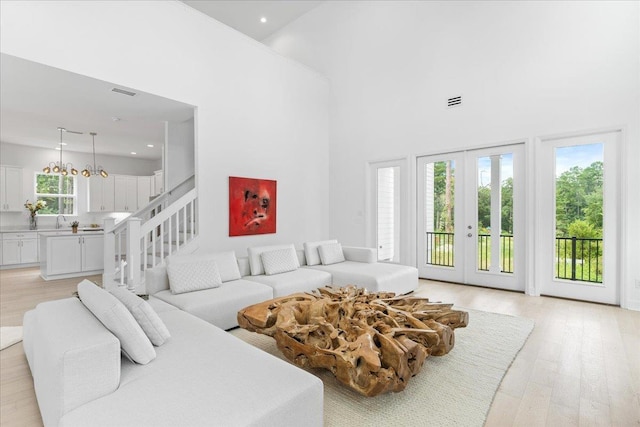 living area featuring a towering ceiling, light wood finished floors, stairs, french doors, and recessed lighting