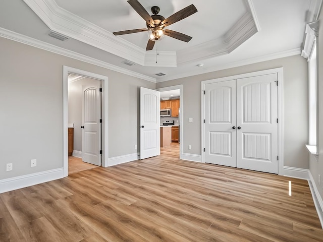 unfurnished bedroom with ornamental molding, light wood-type flooring, ceiling fan, and a raised ceiling