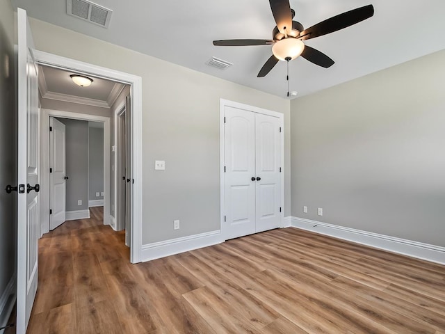 unfurnished bedroom with wood-type flooring, ceiling fan, crown molding, and a closet