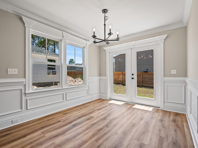 unfurnished dining area with ornamental molding, french doors, light wood-type flooring, and an inviting chandelier