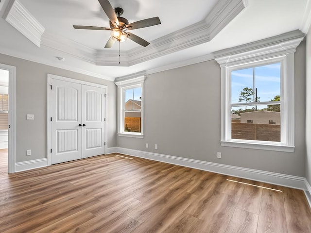 unfurnished bedroom with a raised ceiling, wood-type flooring, ceiling fan, and crown molding