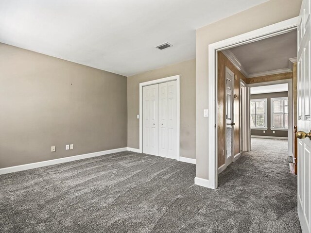 unfurnished bedroom featuring a closet, dark colored carpet, and crown molding