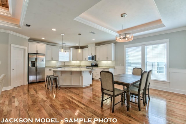 dining area featuring a chandelier, sink, crown molding, a raised ceiling, and light wood-type flooring