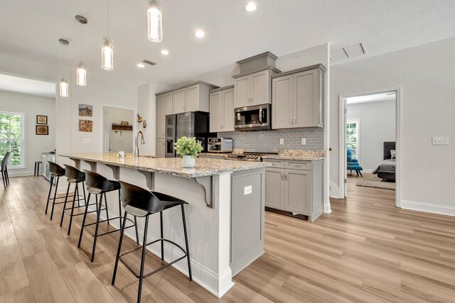 323 Carr Ln, Tallahassee, FL 32312 - kitchen featuring stainless steel appliances, gray cabinets, a breakfast bar area, a large island with sink, and light wood-style floors
