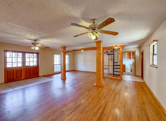 interior space featuring ornate columns, ceiling fan, french doors, a textured ceiling, and light wood-type flooring