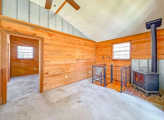 interior space featuring a wood stove, ceiling fan, wood walls, carpet floors, and lofted ceiling