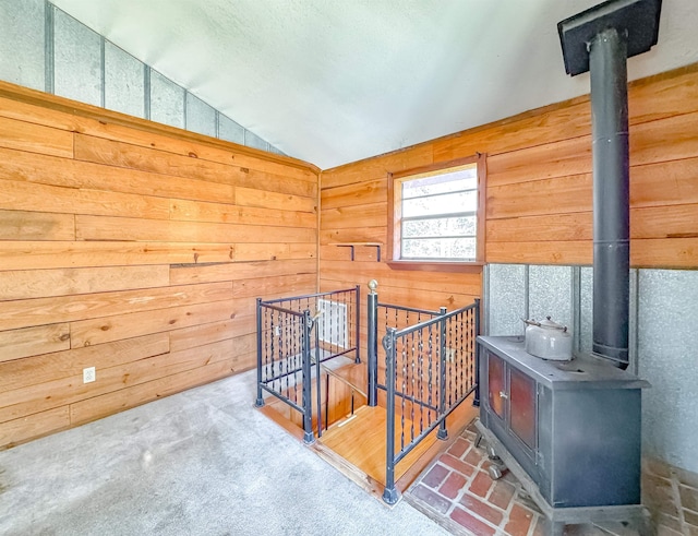 interior space featuring a wood stove, wooden walls, carpet, and vaulted ceiling