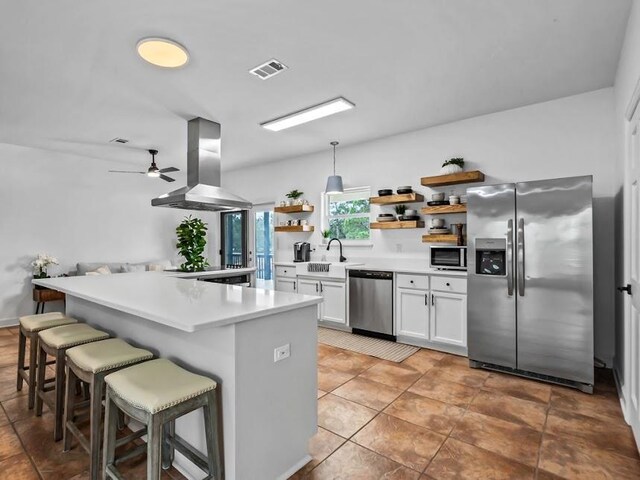 kitchen featuring a kitchen bar, island exhaust hood, stainless steel appliances, white cabinets, and hanging light fixtures