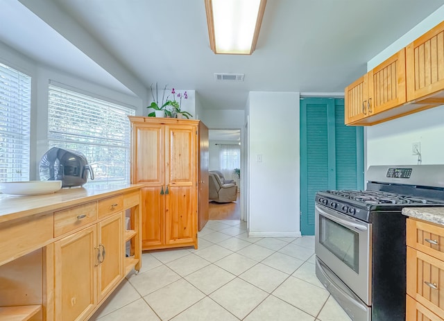 kitchen with stainless steel gas range oven, light tile patterned flooring, and light brown cabinetry