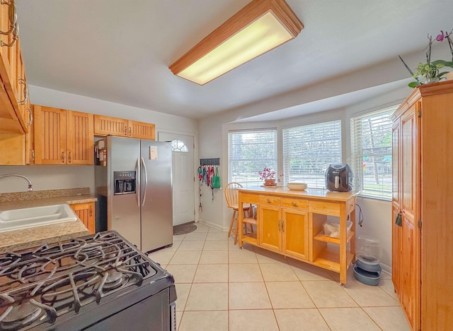 kitchen with stainless steel fridge with ice dispenser, sink, light tile patterned floors, and range with gas stovetop