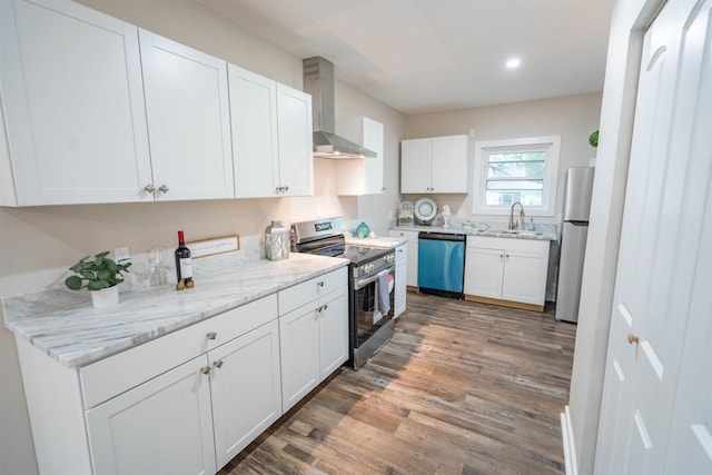 kitchen with appliances with stainless steel finishes, wall chimney exhaust hood, sink, wood-type flooring, and white cabinets