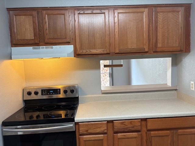 2020 Continental Ave Unit 120, Tallahassee, FL 32304 - kitchen featuring stainless steel electric stove, under cabinet range hood, brown cabinetry, light countertops, and a textured wall