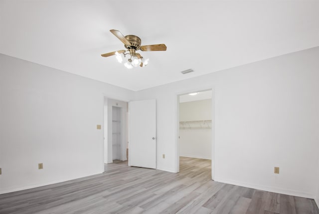 unfurnished bedroom with a spacious closet, light hardwood / wood-style flooring, a closet, and ceiling fan