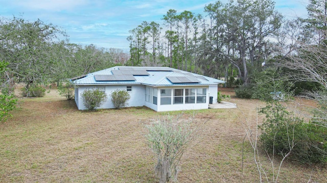 back of property with a sunroom, a lawn, and solar panels