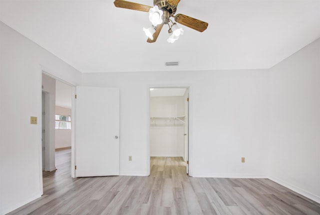 unfurnished bedroom featuring a spacious closet, a closet, ceiling fan, and light wood-type flooring