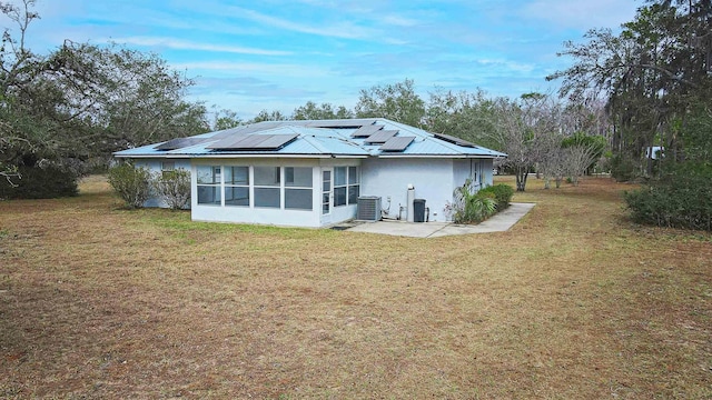 back of property with central AC unit, a yard, a sunroom, and solar panels