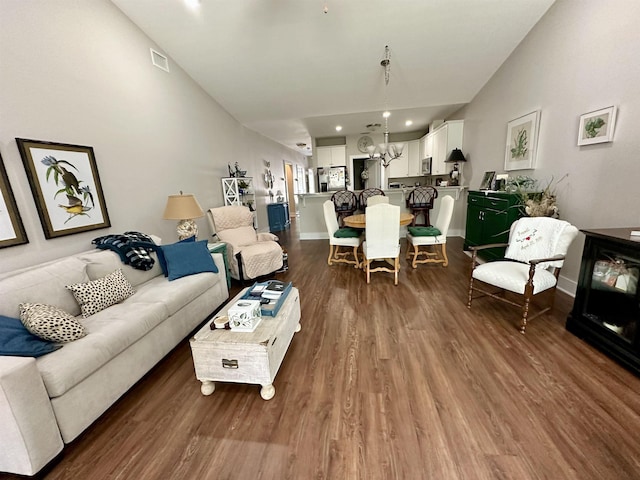 living room featuring dark wood-type flooring, a chandelier, and high vaulted ceiling