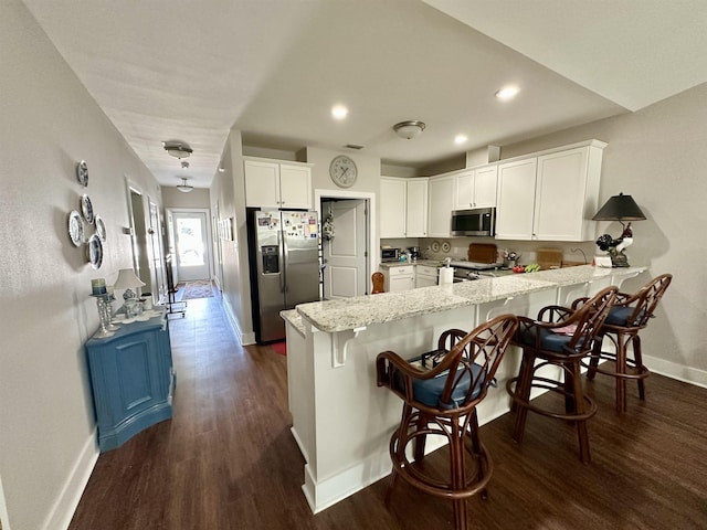 kitchen with a kitchen bar, dark hardwood / wood-style floors, kitchen peninsula, stainless steel appliances, and white cabinets